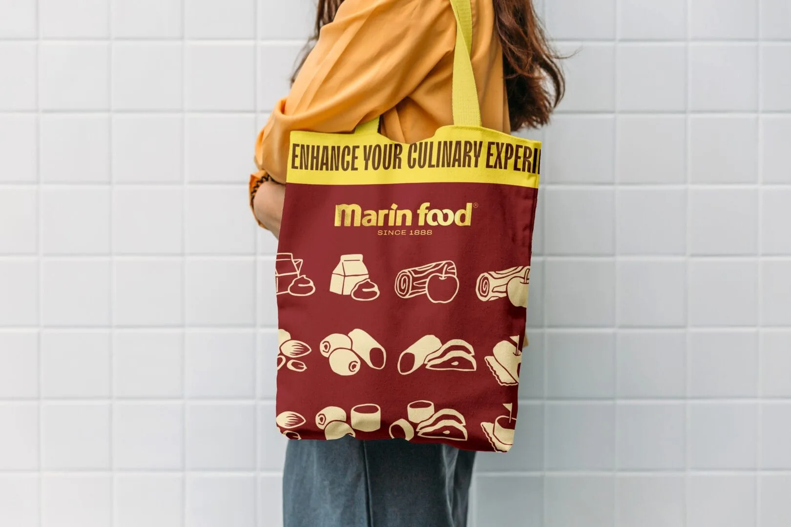 Marin Food illustrated burgundy tote bag carried in front of a tiled wall