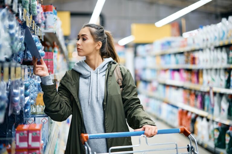 Young woman looking at price tag of hygiene products in supermarket.